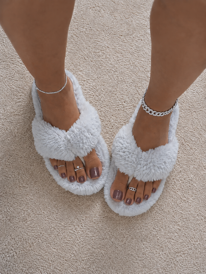 Close-up of feet with dusky pink glitter press-on toenails in white fluffy slippers with silver anklets